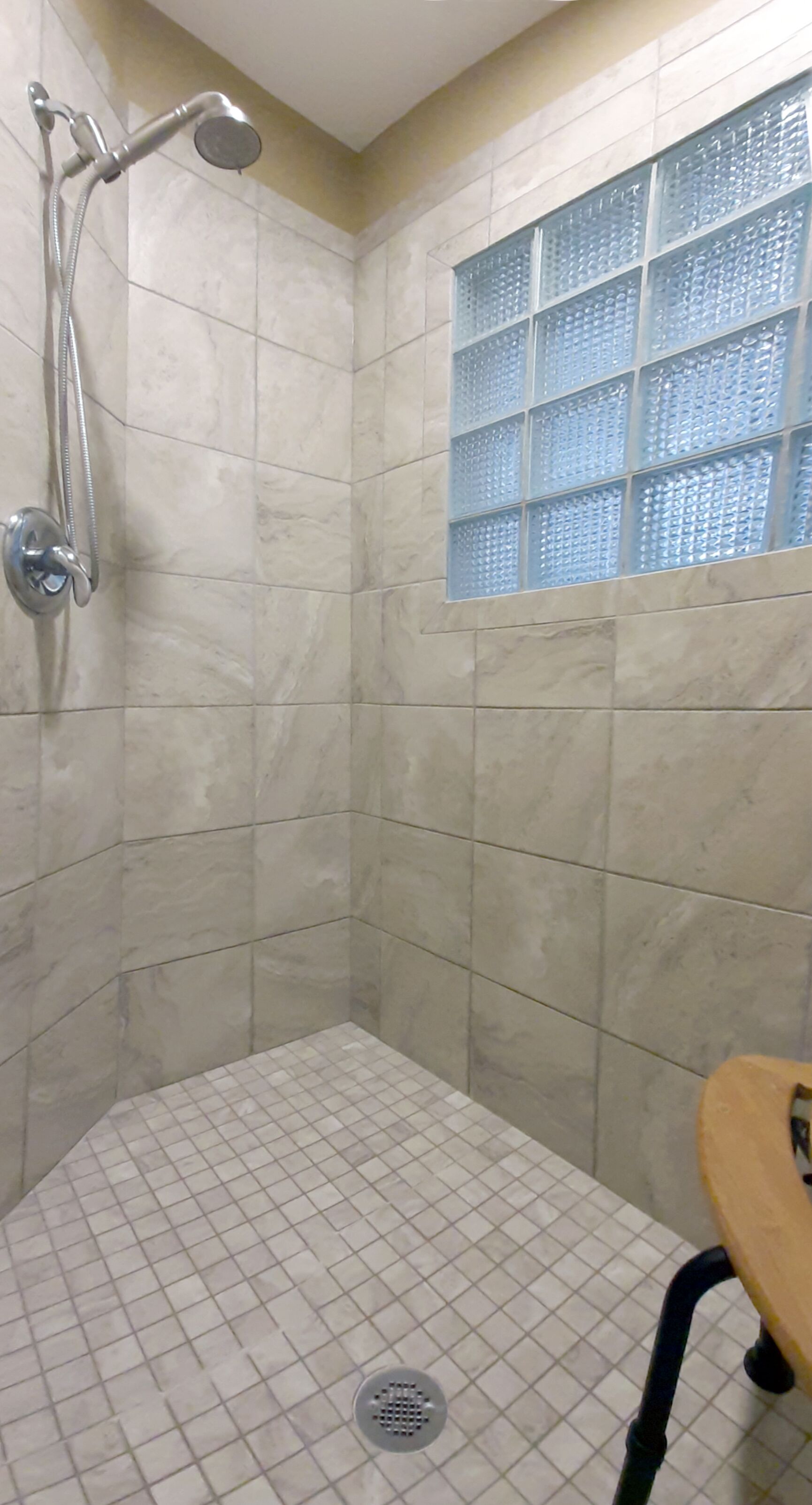 A shower area with a tiled floor, a showerhead, and a window with a grid pattern.