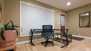 A room with a wooden floor, a black office chair, a glass desk, a pink plant, a closed white door, and a mirror on the wall. - Recliners. Single Level Living. Walk-in shower. (Rochester)