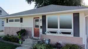 A single-story house with a red door, a front porch, and a small front yard. - Recliners. Single Level Living. Walk-in shower. (Rochester)