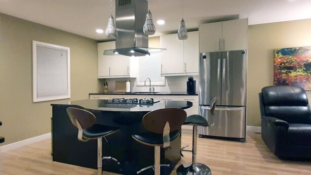 A modern kitchen with a central island, bar stools, stainless steel appliances, and a black leather chair. - Recliners. Single Level Living. Walk-in shower. (Rochester)