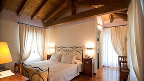 A bedroom with a wooden ceiling, a bed with a metal frame, two bedside tables with lamps, and curtains on the windows. - Casa Orter (Pavia di Udine)