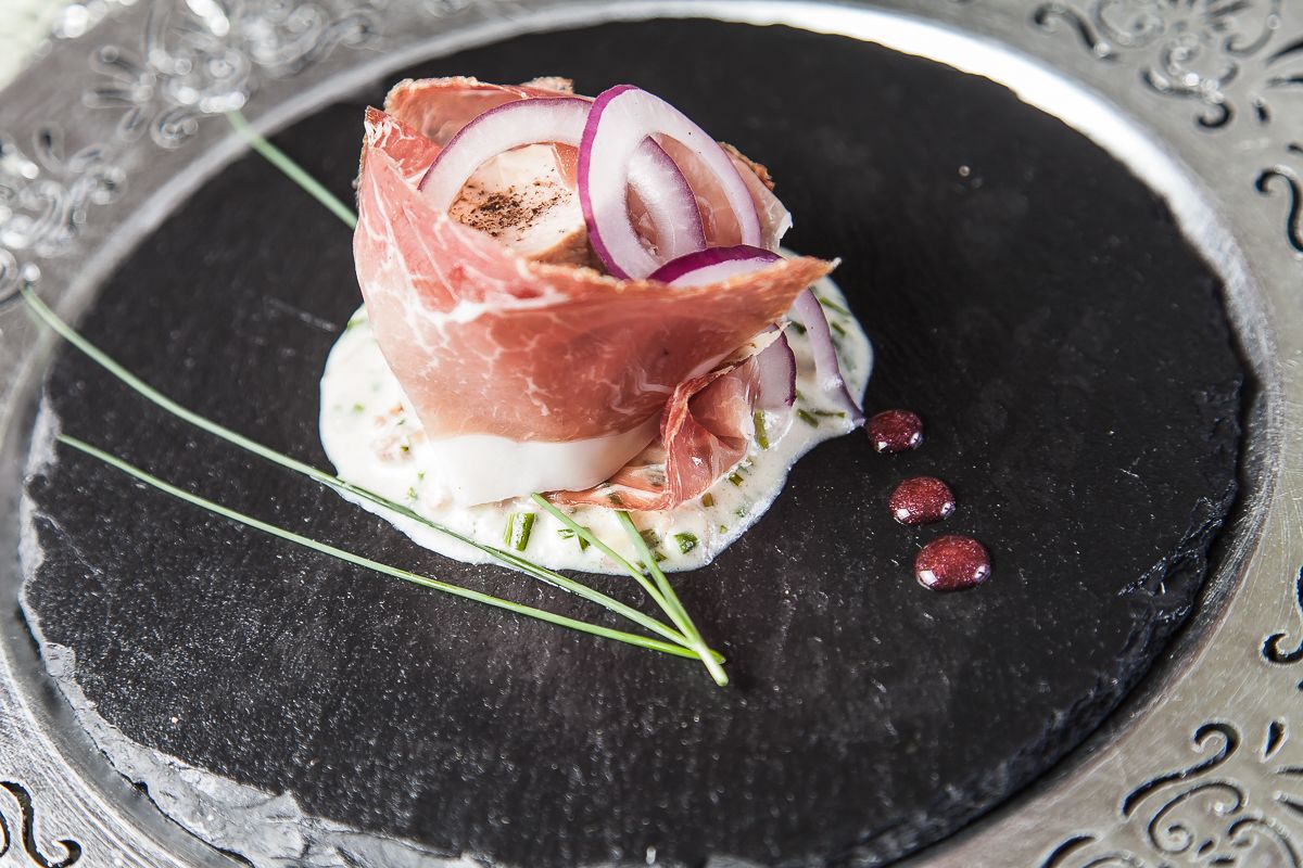 Un piatto con prosciutto, cipolla rossa e salsa cremosa.