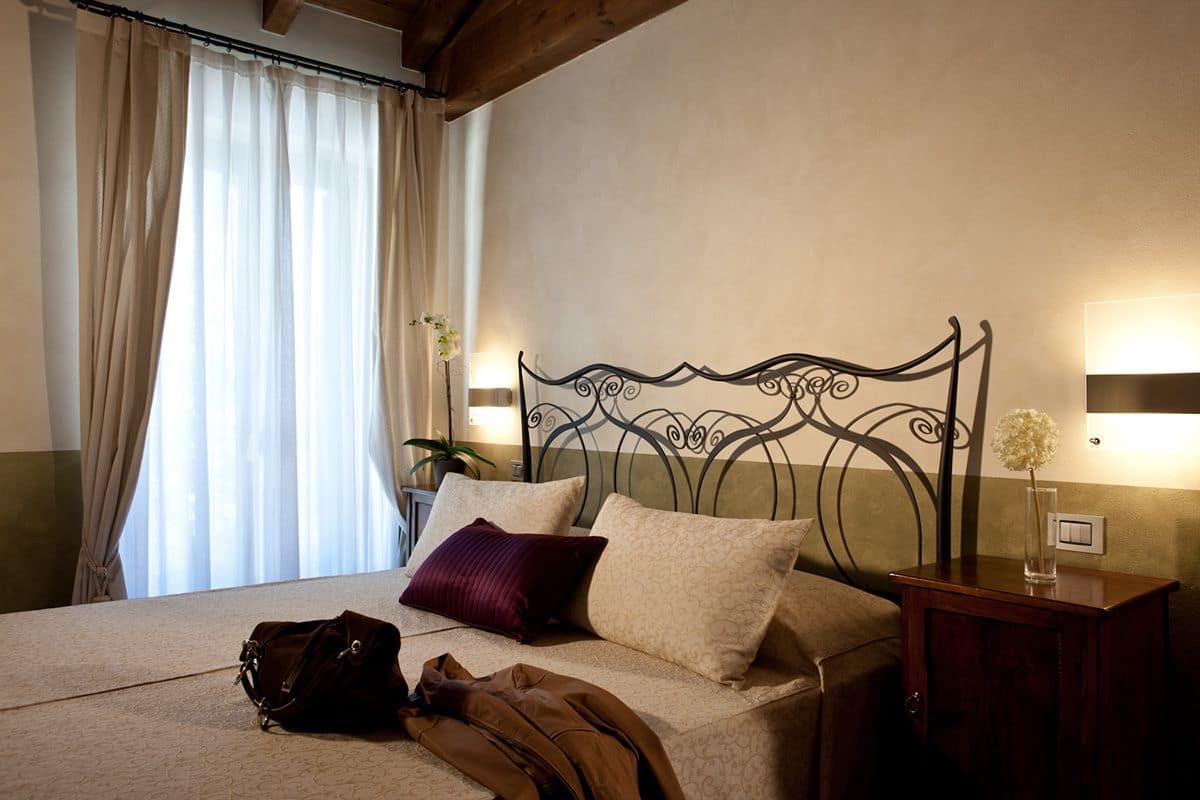 Une chambre d’hôtel avec un lit, une table de chevet, une lampe et une fenêtre avec des rideaux.