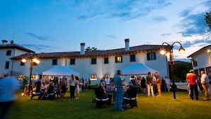An outdoor gathering with people seated at tables under tents, with buildings in the background. - Casa Orter (Pavia di Udine)