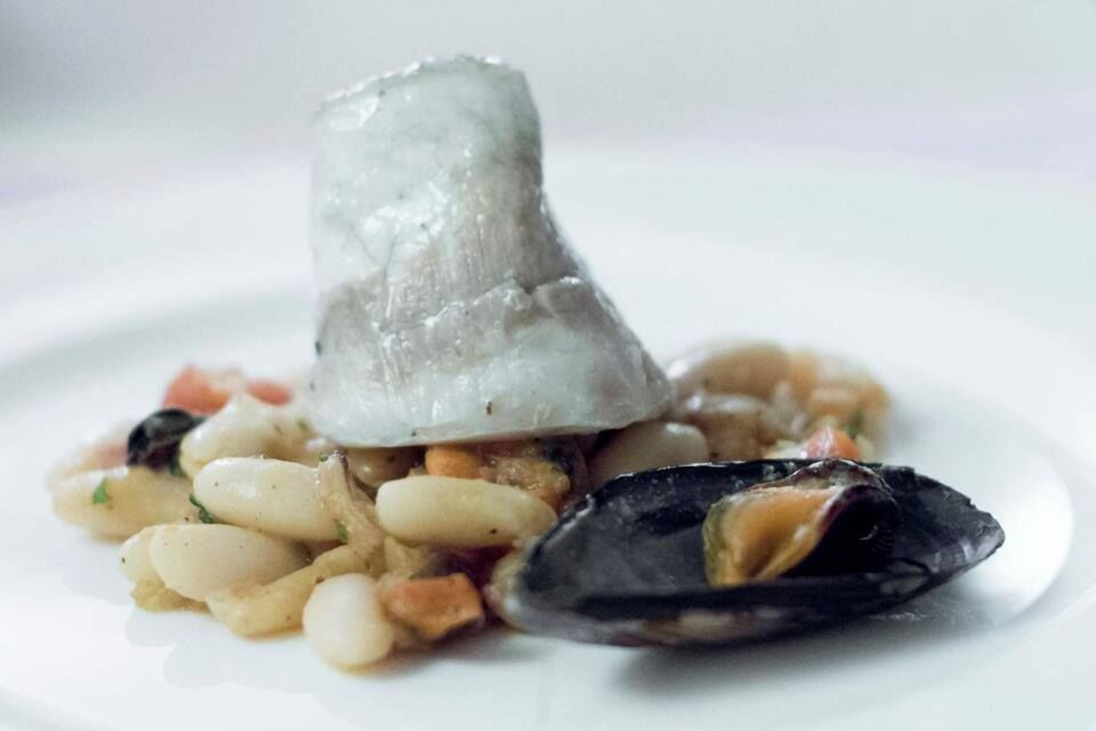 Ein Fischgericht mit Muscheln und weißen Bohnen auf einem Teller.