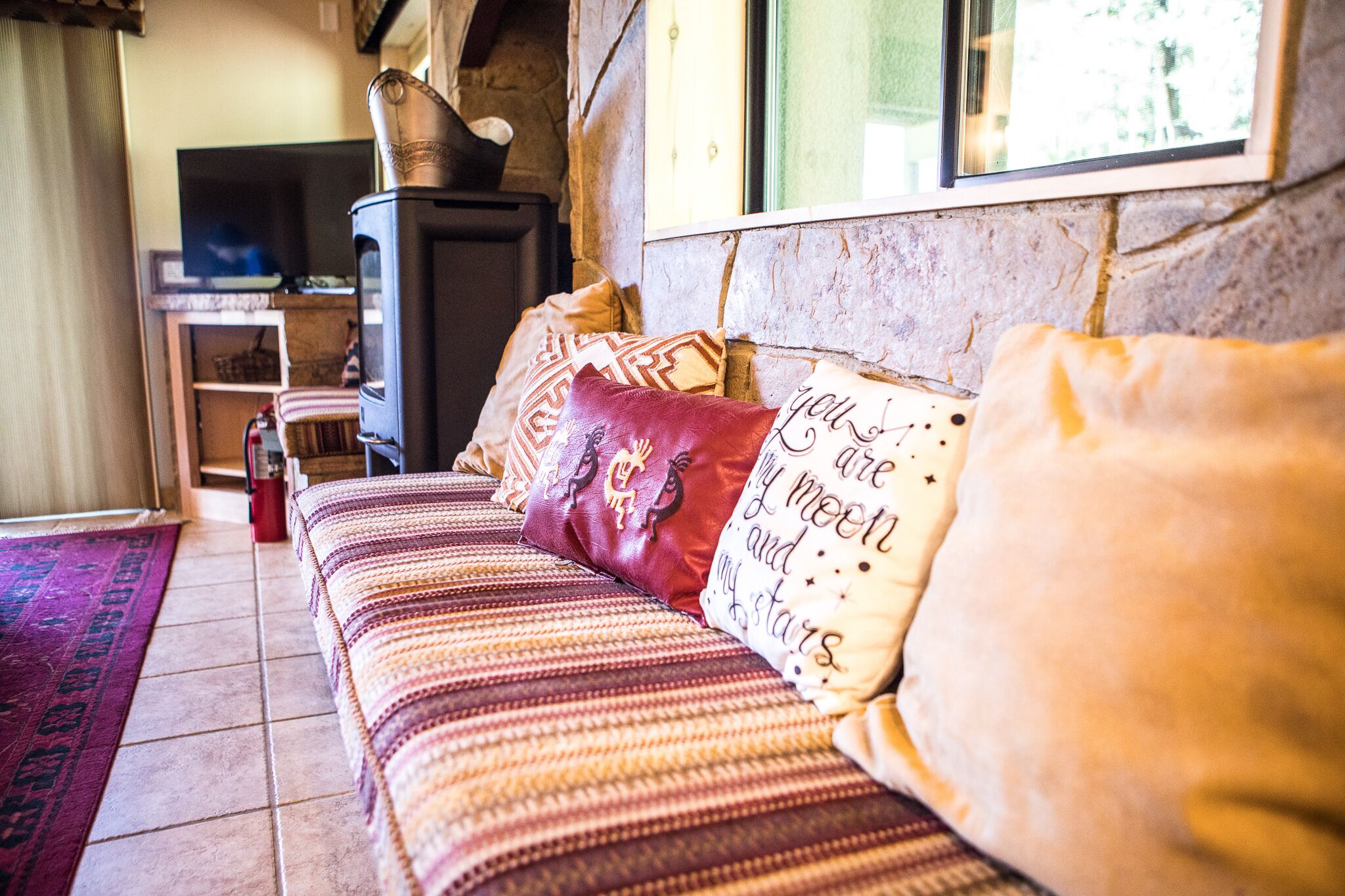 Un salon chaleureux avec un canapé, des coussins à motifs, un téléviseur et une cheminée en pierre.