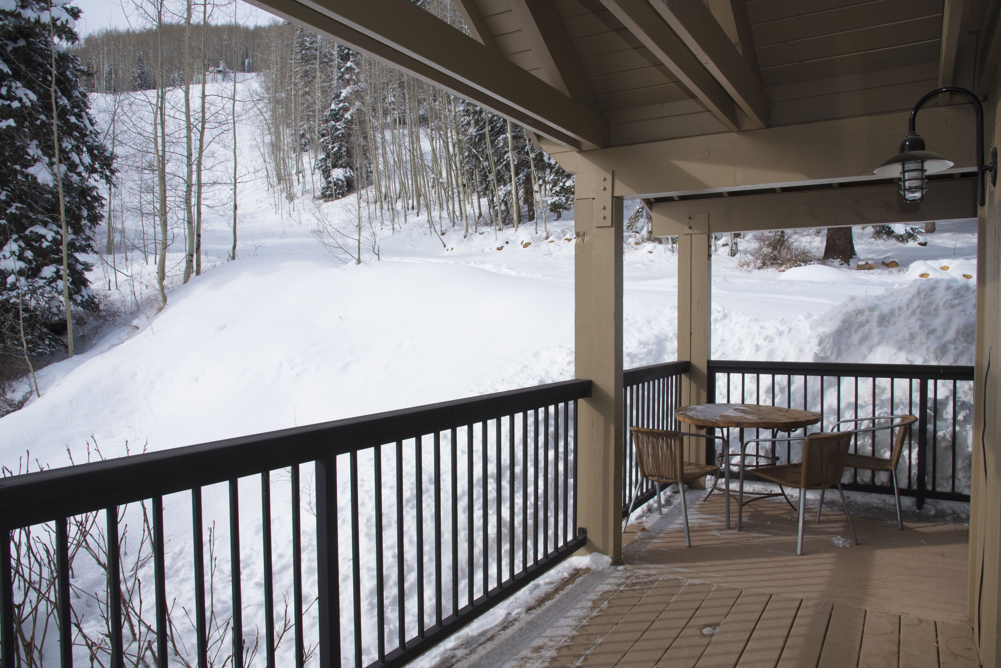 Un espace extérieur abrité, doté d’une terrasse en bois, d’une rambarde en métal et d’une table avec des chaises.