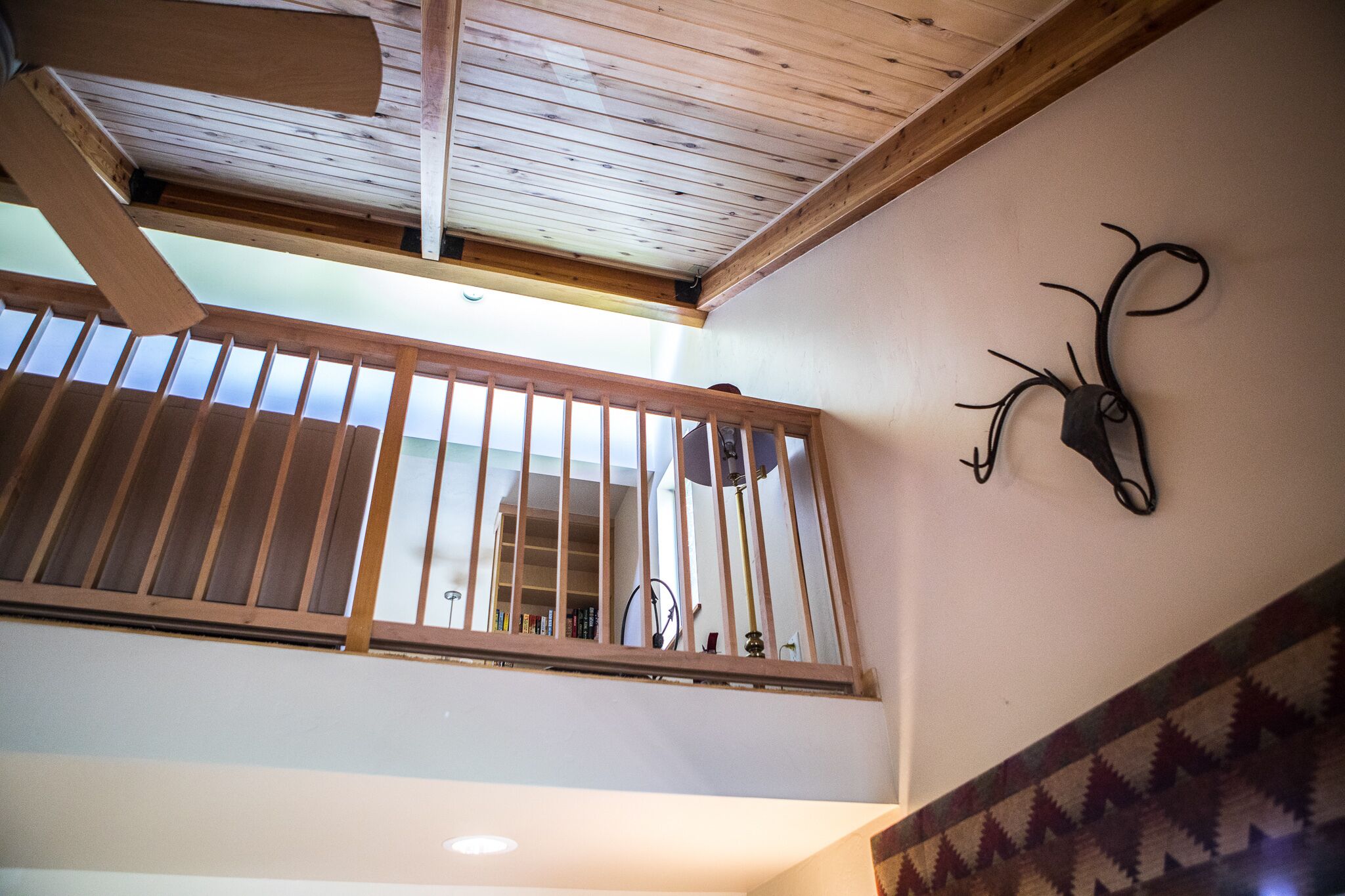 Un balcon en bois avec une rambarde en métal, un ventilateur de plafond et une décoration murale représentant une tête de cerf.
