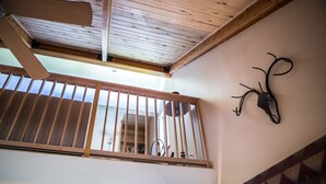 A wooden balcony with a metal railing, a ceiling fan, and a wall-mounted deer head decoration.
