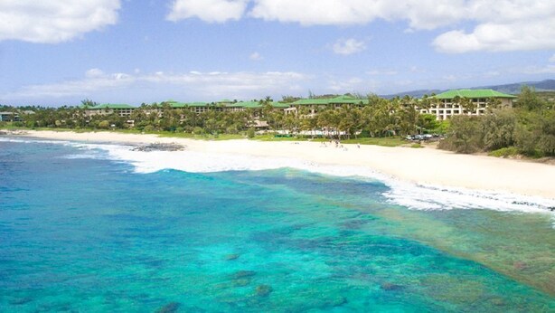 Un resort en la playa con aguas turquesas cristalinas, playas de arena blanca y una hilera de edificios con techos verdes.