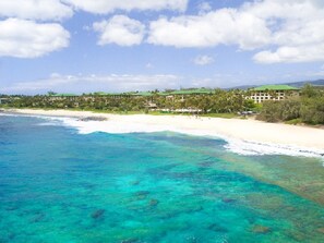 A beach resort with clear turquoise waters, white sandy beaches, and a row of buildings with green roofs.