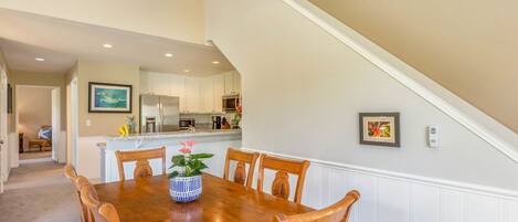 A dining area with a wooden table and chairs, a ceiling fan, and a kitchen in the background.