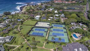 Vista aérea de una zona residencial con varias canchas de tenis, una piscina y casas con vistas al océano.