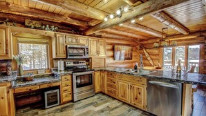 A rustic kitchen with wooden cabinets, a built-in microwave, stainless steel appliances, and a large window overlooking a snowy landscape.