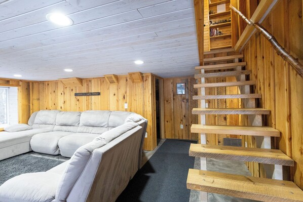 Un interior de madera con un sofá modular, una escalera y un cartel que dice 'Disfruta de las cosas sencillas'.