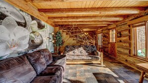 A log cabin interior with a leather sofa, a stone fireplace, and a wooden staircase.