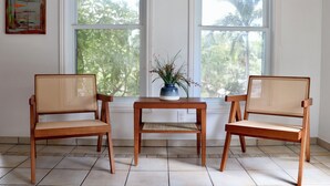 A room with three wooden chairs and a table, a potted plant, and a window with a view of trees. - Crescent 1 Grace Bay Beach (Providenciales)