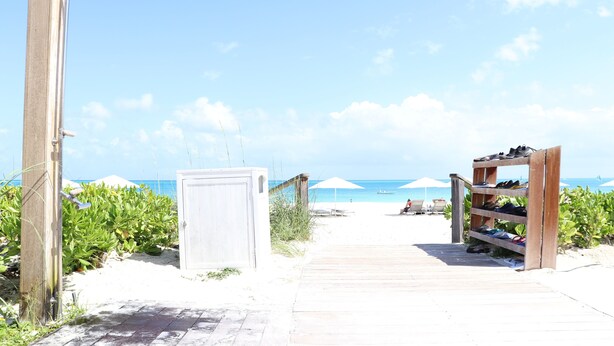 A wooden boardwalk leading to a beach with umbrellas and a shoe rack. - Crescent 1 Grace Bay Beach (Providenciales)