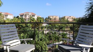 A balcony with two white lounge chairs, a view of buildings with red roofs, and lush greenery. - Crescent 1 Grace Bay Beach (Providenciales)