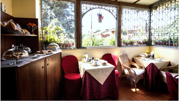Comedor con una mesa lista para dos, sillas rojas y vista al jardín a través de una ventana con barandilla de hierro decorativa.