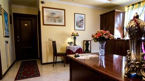 Un pasillo con puerta de madera, alfombra roja, una mesa con lámpara y flores, y una estatua decorativa.