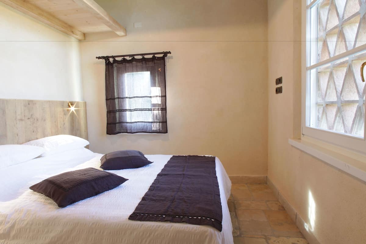 A bedroom with two beds, a window with a decorative screen, and a stone floor.