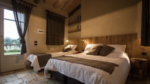 A bedroom with two beds, a stone floor, wooden headboard, and a window with curtains. - Olimagio (Pietrasanta)