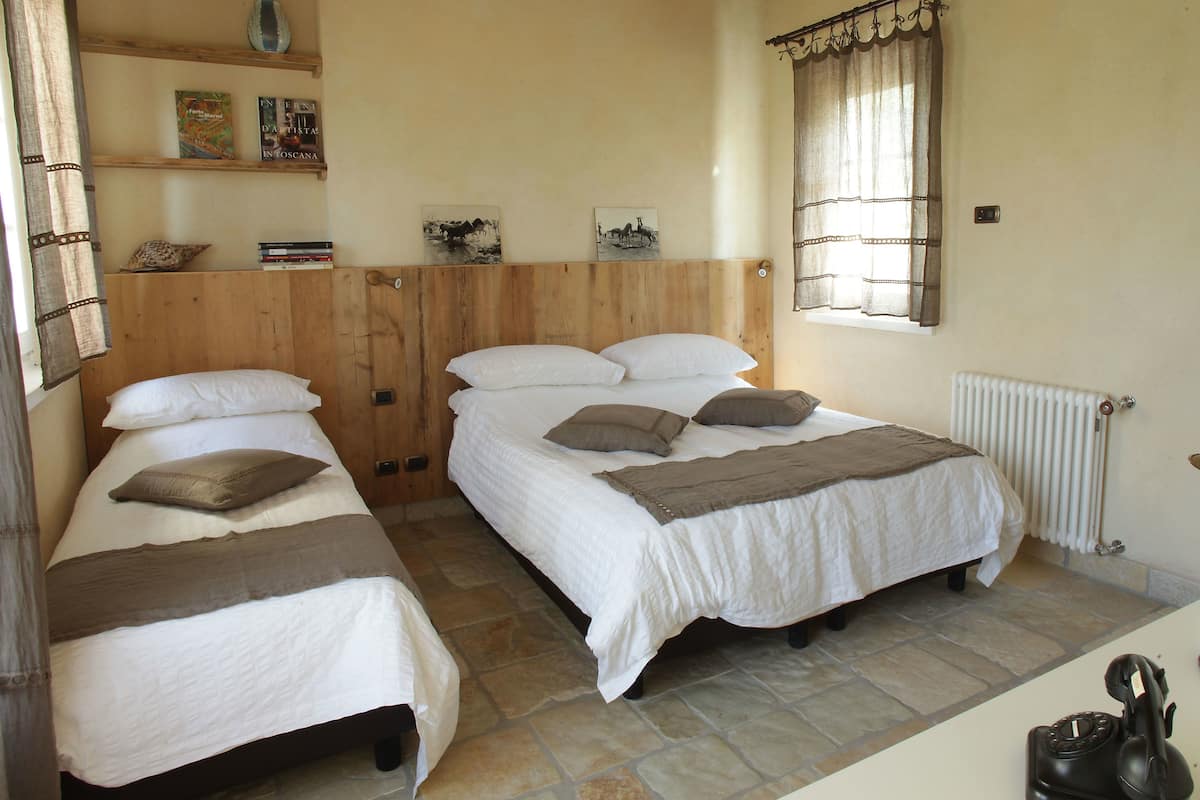 A bedroom with two single beds, a wooden headboard, a radiator, and a window with curtains.