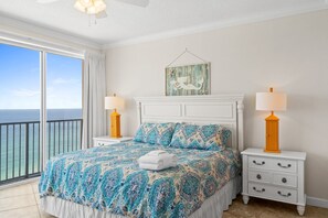A bedroom with a large bed, two bedside tables with lamps, a white dresser, and a view of the ocean. - Boardwalk Beach Resort Condo w/ Stunning Gulf Views (Panama City Beach)