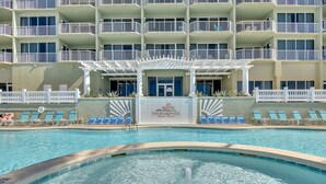 A hotel pool area with a clear view of the pool, lounge chairs, and a building with multiple balconies.