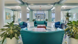 A lobby with teal sofas, a coffee table, potted plants, and a large entrance door.