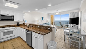 A kitchen with white cabinets, a granite countertop, and a view of the ocean through a sliding glass door.