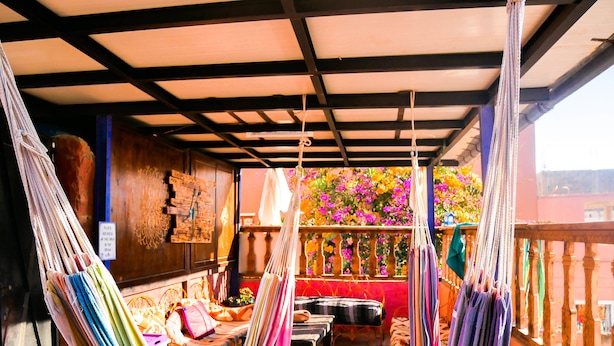 Ein Zimmer mit Hängematten, einem Holztisch und Blick auf bunte Blumen.