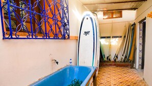 Ein schmaler Flur mit einer blauen Badewanne, einem Wasserhahn und einer Reihe von Surfbrettern, die an der Wand lehnen.