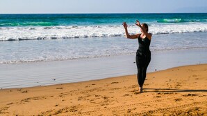 Eine Person am sandigen Strand, im Hintergrund Wellen.