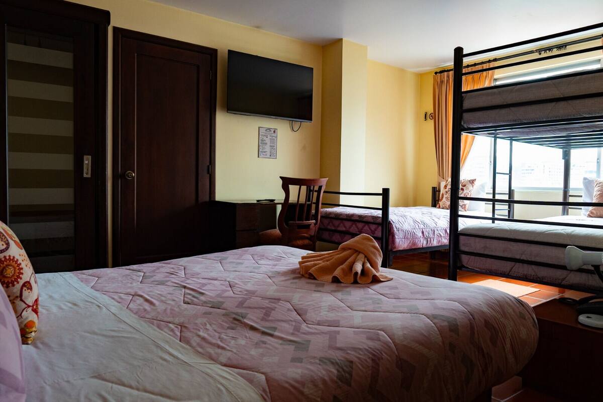 A hotel room with a bunk bed, a desk, a chair, a television, and a window with curtains.