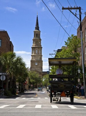 A street with a historic clock tower, a horse-drawn carriage, and a crosswalk.