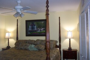 A bedroom with a four-poster bed, two bedside lamps, a ceiling fan, and a framed picture on the wall.