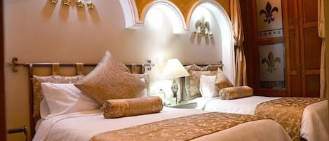 Habitación de hotel con dos camas, una araña y paneles decorativos en las paredes.