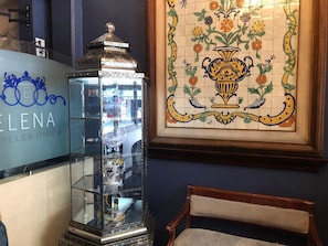 A glass display case with decorative items, a framed tile mural, and a wooden chair. - Hotel Elena (Puebla)