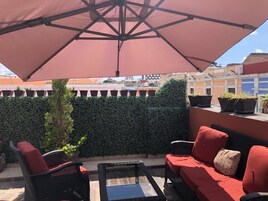 Een terras op het dak met buitenmeubilair, een grote parasol en potplanten.