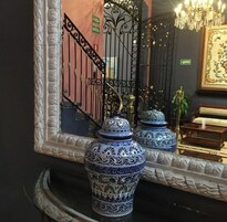 Een spiegel reflecteert een wenteltrap met sierlijke metalen leuningen, een kroonluchter en decoratieve vazen.