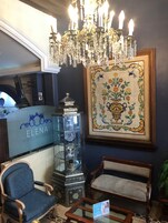 Een hal met een kroonluchter, een receptiebalie met de naam 'ELENA', een glazen vitrine met porselein en een lijst met een bloementegel.