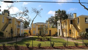 A yellow building with a symmetrical facade, a central entrance, and a well-maintained lawn.