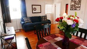 A living room with a sofa, a coffee table, and a dining table with chairs. There is a vase with flowers on the dining table.