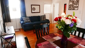 A living room with a sofa, a coffee table, and a dining table with chairs. There is a vase with flowers on the dining table. - C1, Perfect location in city center with balcony, near beaches, free parking! (St. Augustine)