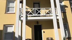 A two-story building with a balcony, white columns, and a black door.