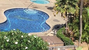 Une piscine à bords ondulés, entourée de verdure et agrémentée de deux barbecues.