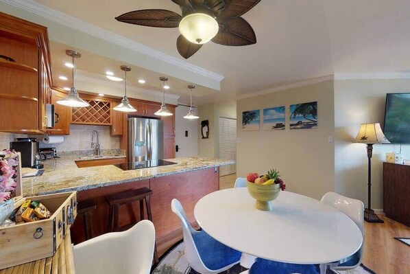 A modern kitchen with wooden cabinets, a central island, pendant lights, and a ceiling fan.