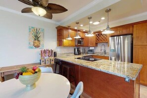 A kitchen with wooden cabinets, a stainless steel refrigerator, a granite countertop, and pendant lighting.